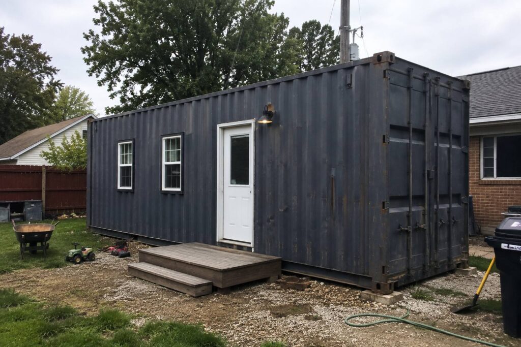 Shipping container converted into a backyard tiny home with windows and a door