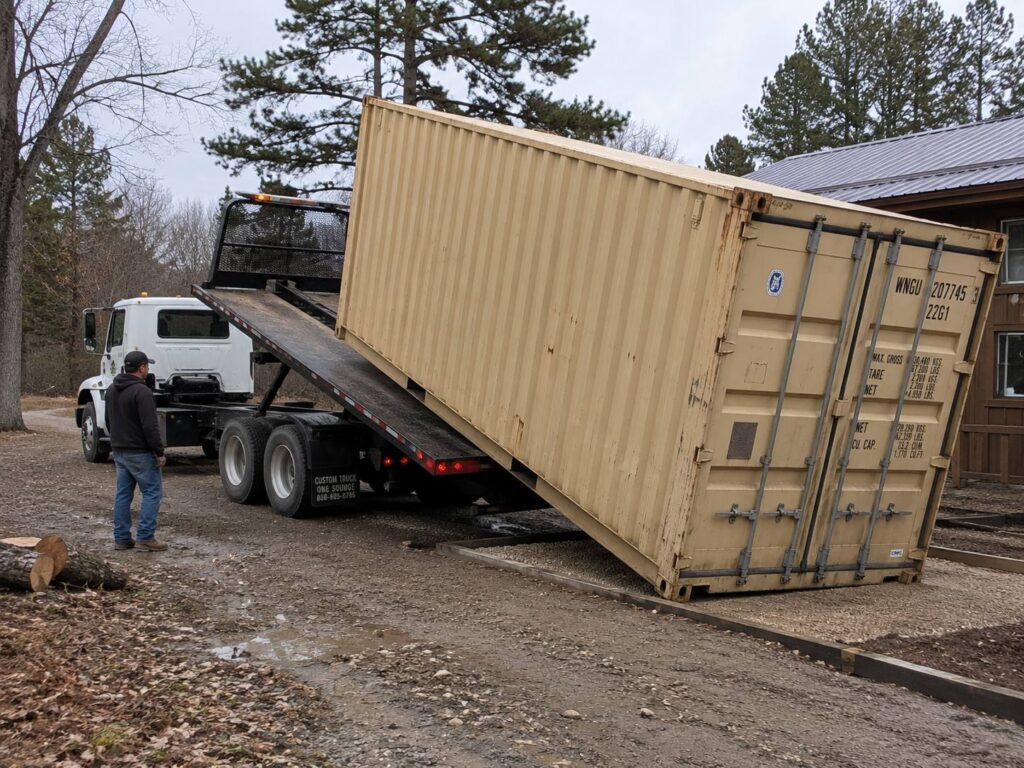 Shipping container being delivered and unloaded from a tilt-bed truck on site